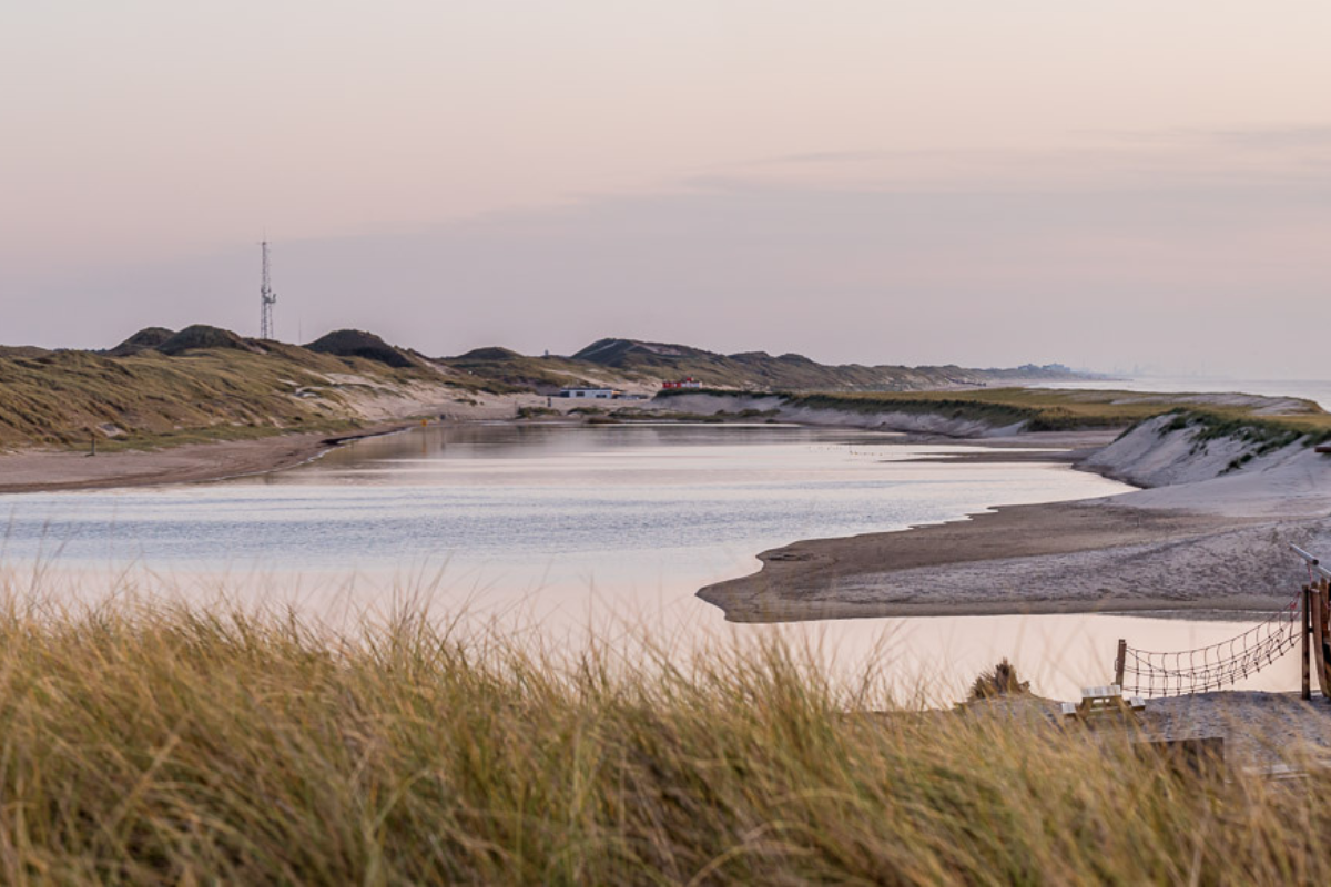 Foto van de Lagune met roze getinte zonsondergang en op de achtergrond de duinen met duingras